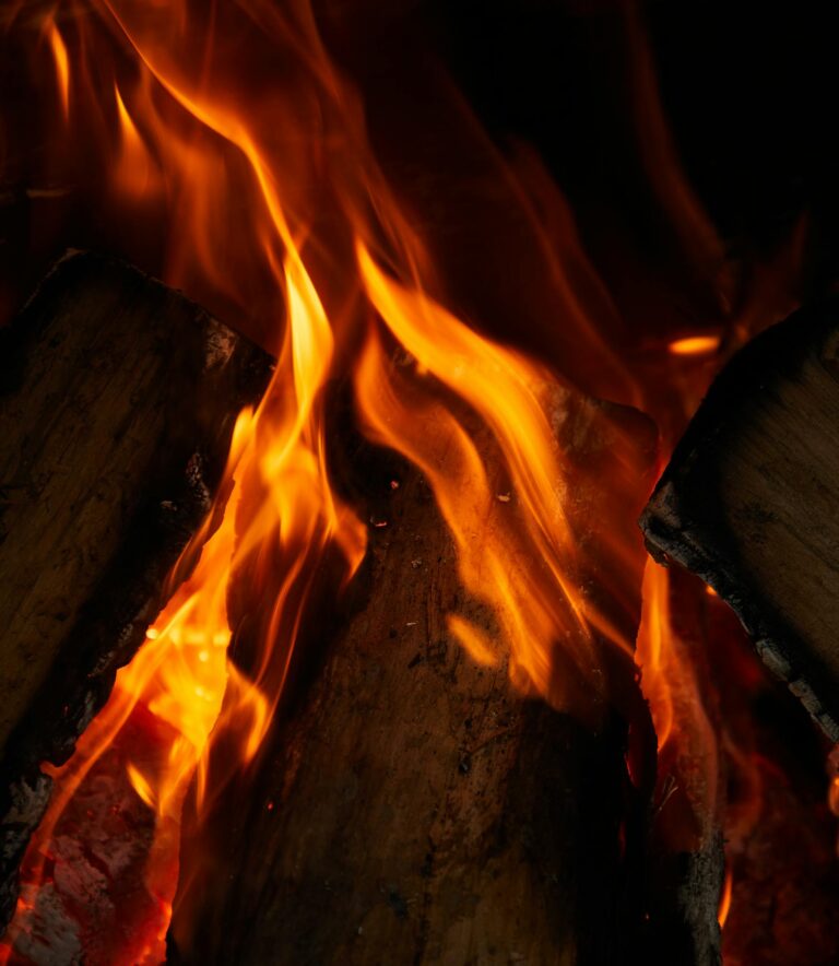 From above closeup of bonfire with bright flame and wood on sandy surface at night